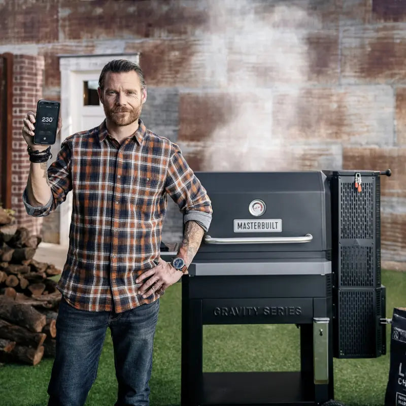 A man in front of a Masterbuilt Gravity Series BBQ with the smart app on his phone to track temperature
