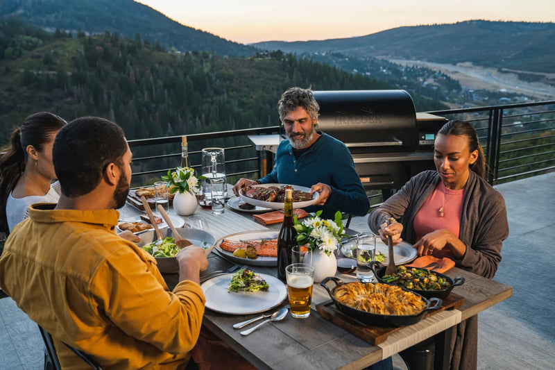 Friends Eating a BBQ feast with a Traeger Grill behind them