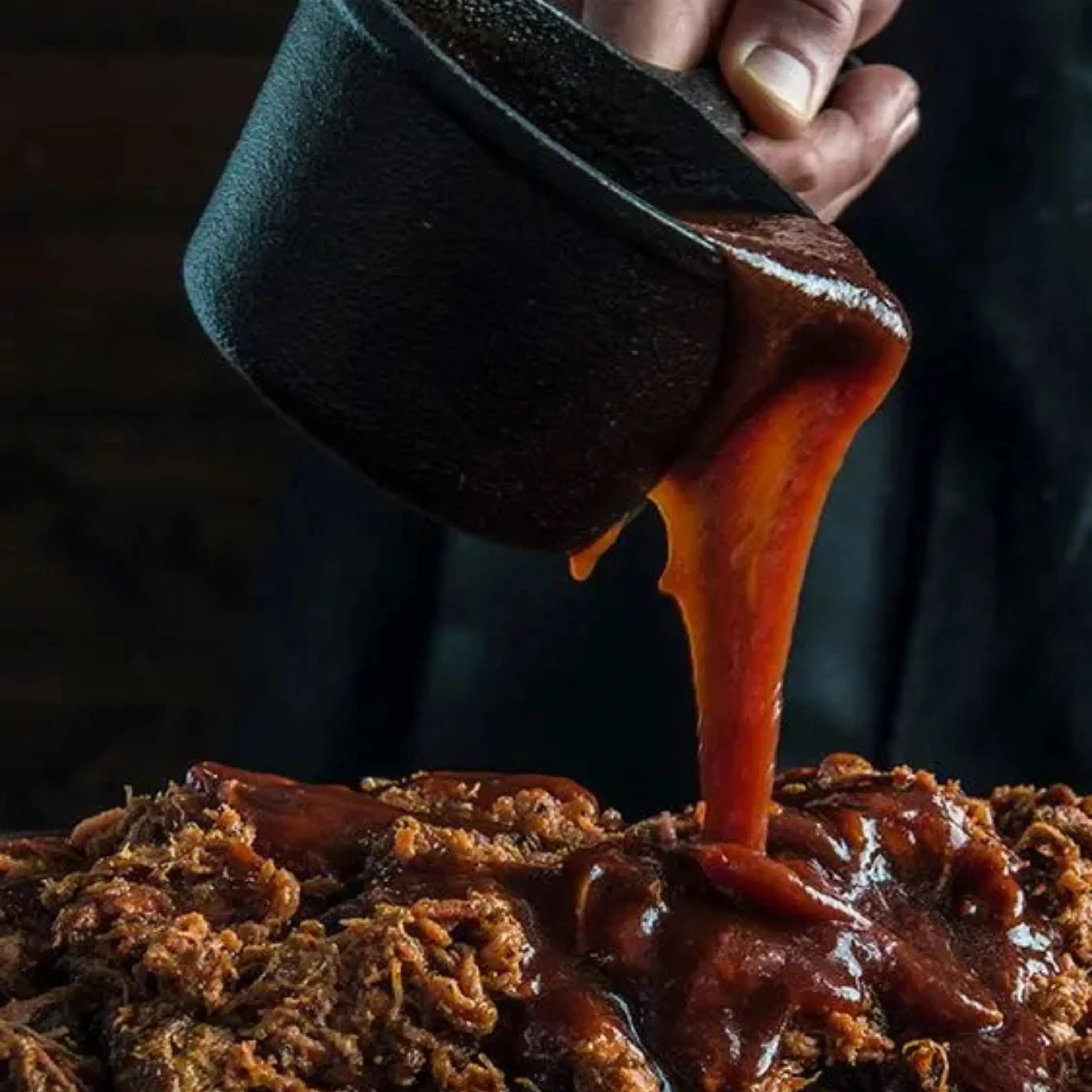 Someone pouring bbq sauce on brisket