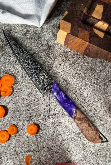 A utility knife with a Damascus steel blade and a wooden handle, resting on a textured surface with carrots nearby.