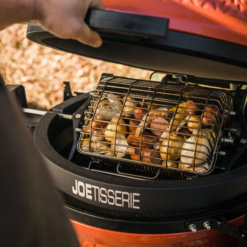 Someone cooking meat and potatoes on a Kamado Joe Joetisserie