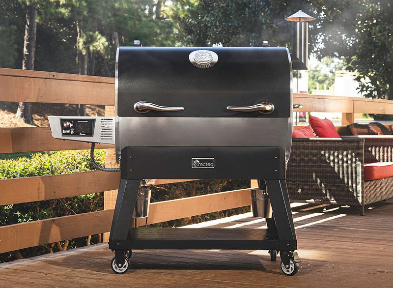 Black barbecue grill on a wooden deck with outdoor furniture and greenery in the background