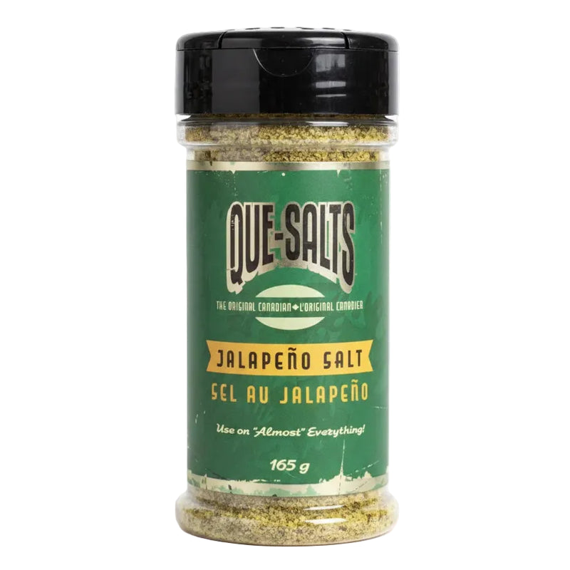 A 165 g plastic shaker bottle of Que-Salts Jalapeño Salt, featuring a green label with white and yellow text and a black flip-top lid, set against a plain white background.